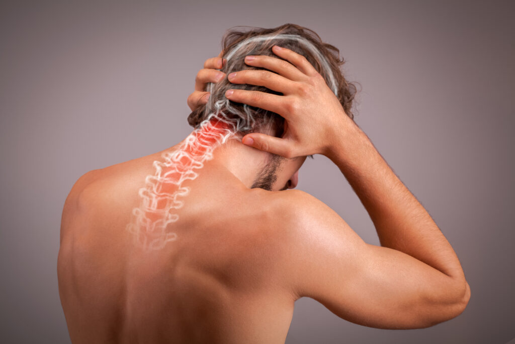 Man holding the back of his neck in pain, with the cervical spine highlighted